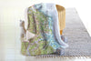 Map-patterned throw blanket draped over a chair with a basket and toys on a light wooden floor.