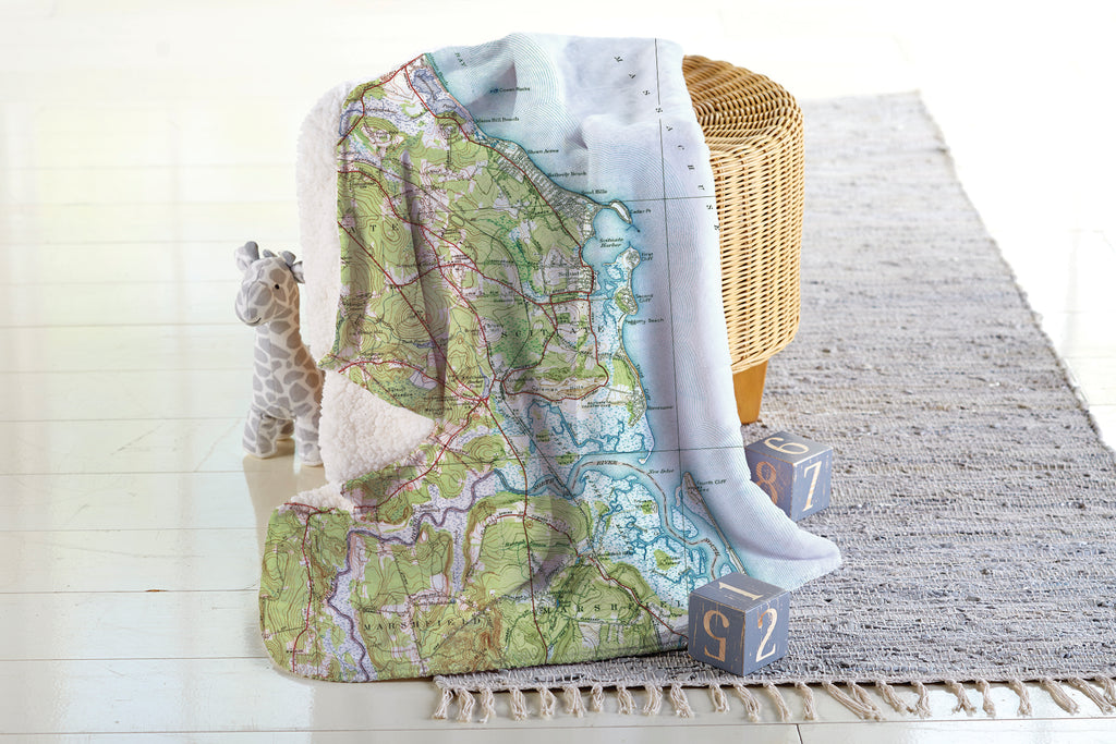 Map-patterned throw blanket draped over a chair with a basket and toys on a light wooden floor.