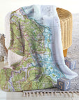 Map-patterned throw blanket draped over a chair with a basket and toys on a light wooden floor.