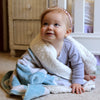 Baby wrapped in a soft blanket sitting on a carpeted floor.
