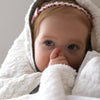 Child wrapped in a white blanket with a pink headband, looking directly at the camera.